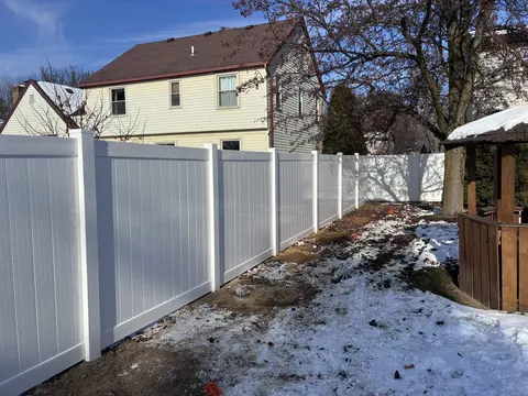White privacy fence beside snow-covered ground and a gazebo.