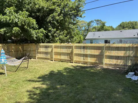 The rails and posts side of a wood privacy fence beside a lawn and hammock.