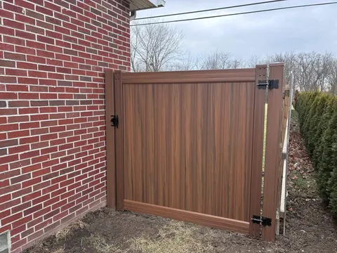 Brown woodgrain-look privacy gate beside a brick wall.